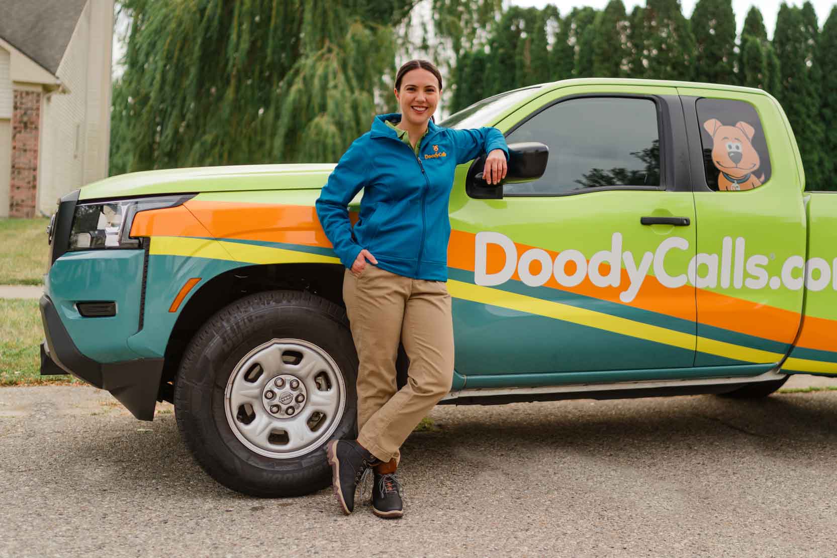 woman in technician uniform leaning against DoodyCalls truck